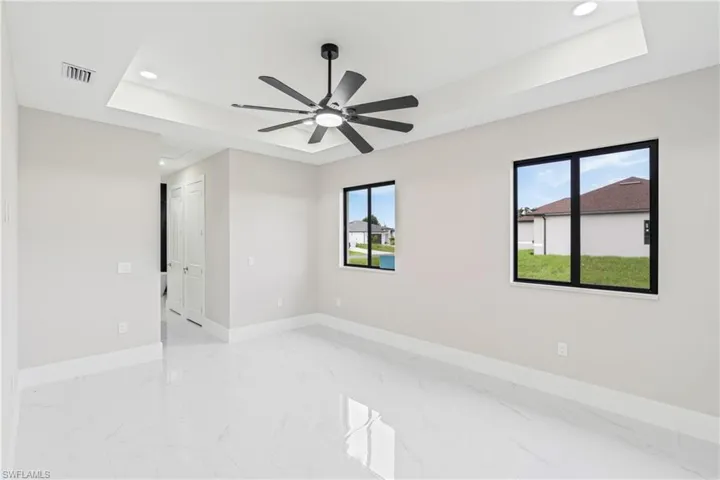 Spare room with a raised ceiling, light marble finish flooring, recessed lighting, and ceiling fan