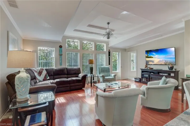 Living room with a raised ceiling, ceiling fan, ornamental molding, and hardwood / wood-style flooring
