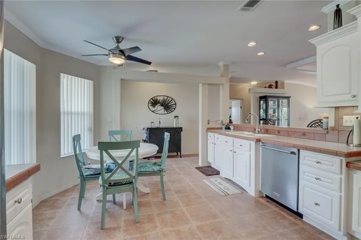 Kitchen featuring tile countertops, white cabinetry, ceiling fan, dishwasher, and sink