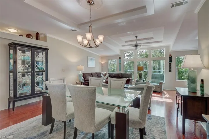 Dining area featuring ceiling fan with notable chandelier, a tray ceiling, light hardwood / wood-style flooring, and crown molding