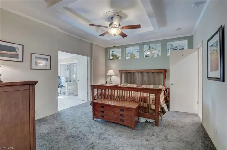 Carpeted bedroom with ceiling fan, ornamental molding, connected bathroom, and a raised ceiling