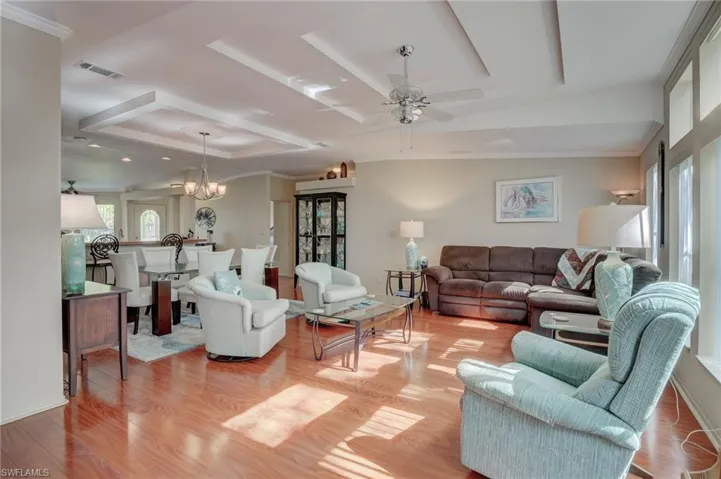 Living room featuring light hardwood / wood-style floors, a tray ceiling, crown molding, and ceiling fan with notable chandelier