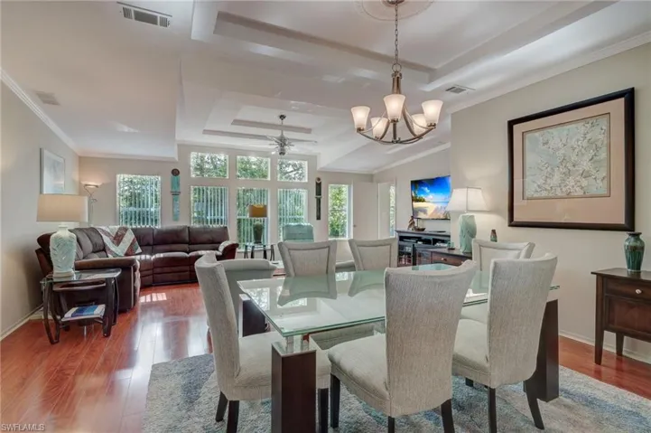 Dining room featuring ceiling fan with notable chandelier, wood-type flooring, ornamental molding, and a raised ceiling