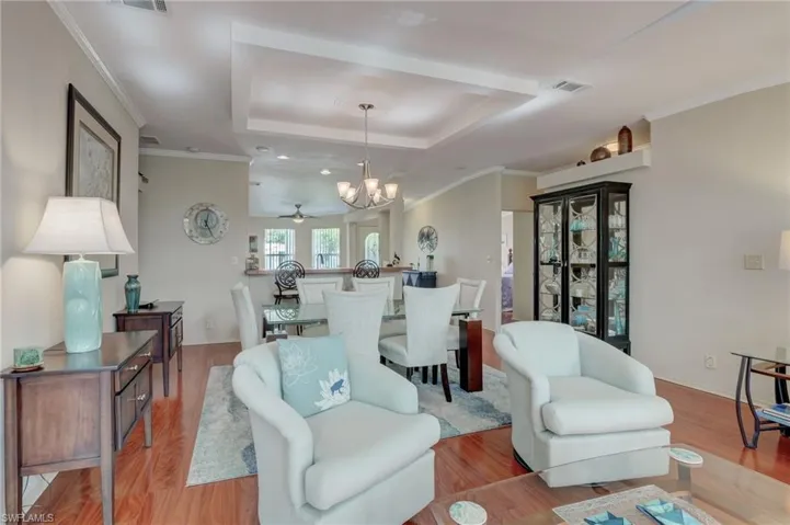Living room with light wood-type flooring, ceiling fan with notable chandelier, a tray ceiling, and ornamental molding