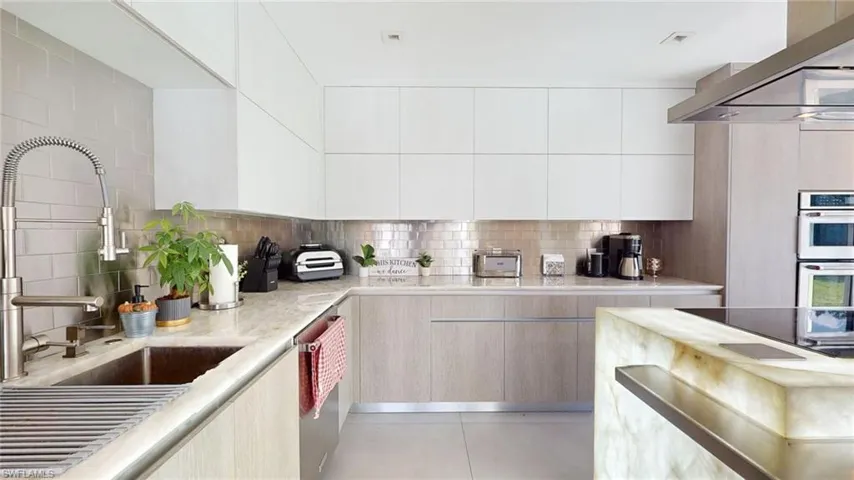 Kitchen featuring tasteful backsplash, wall chimney range hood, light tile patterned floors, and white double oven