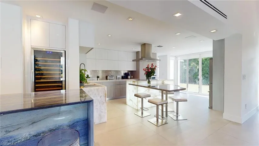 Kitchen featuring tasteful backsplash, white cabinetry, wine cooler, island exhaust hood, and light stone countertops