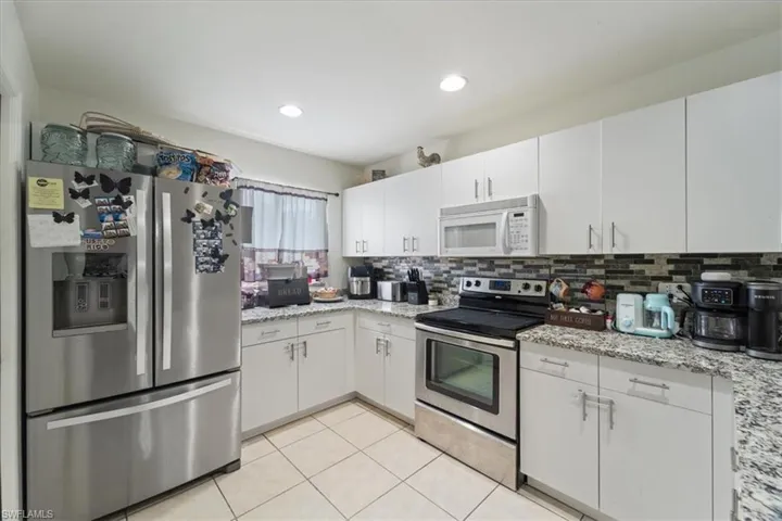 Kitchen featuring white cabinetry, granite countertops, tile flooring, stainless steel appliances, and a mosaic tile backsplash