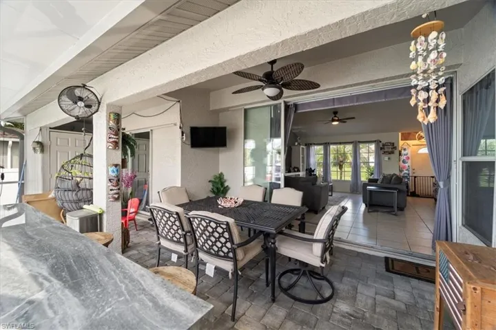 Covered patio with paver flooring, overhead ceiling fan, and bar seating with a stone-finish countertop