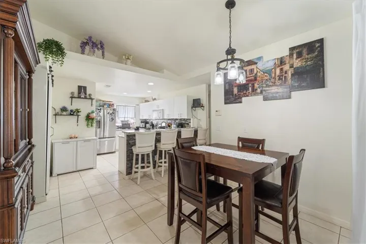 Open-concept dining area featuring a dark wood dining table with seating, tile flooring, and a modern chandelier
