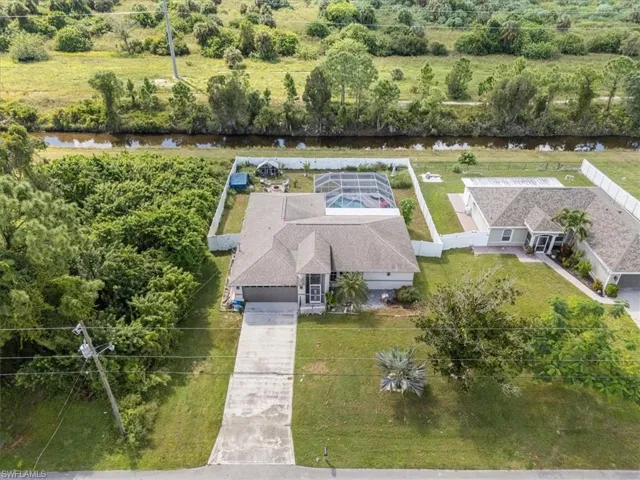 Aerial view showcasing a residential property with a screened swimming pool, an attached garage, and a concrete driveway