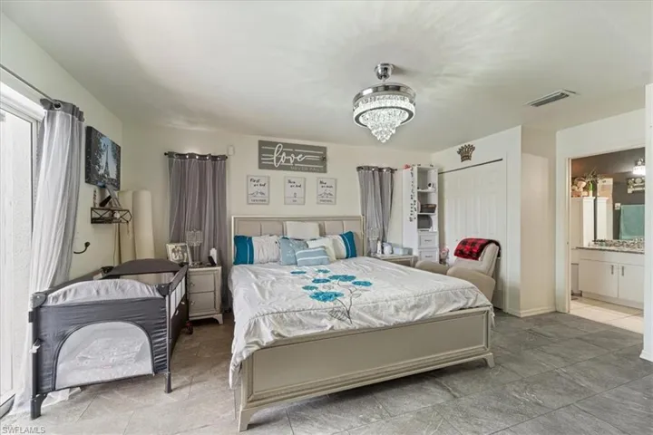 Spacious room featuring gray tile flooring, a crystal chandelier, a white sliding door closet, and an adjacent bathroom with a vanity