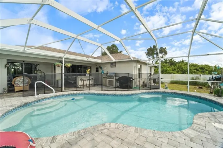 Screened-in outdoor living space featuring a freeform swimming pool with integrated steps, paver decking, and a built-in outdoor kitchen with bar seating