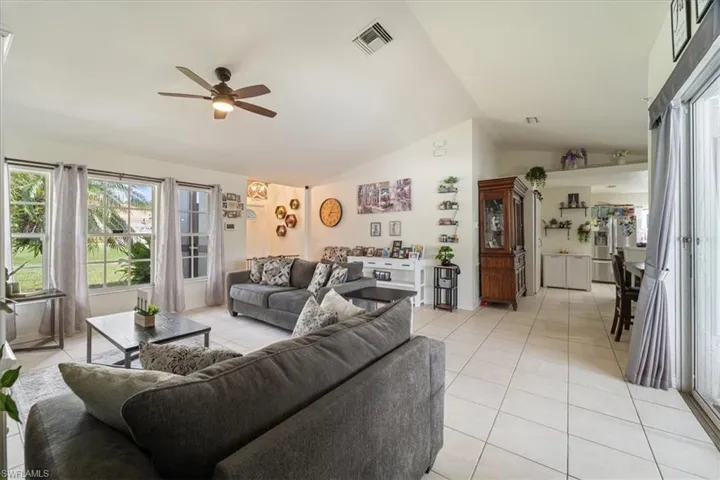 Spacious living area featuring light-toned tile flooring, vaulted ceilings, and a ceiling fan