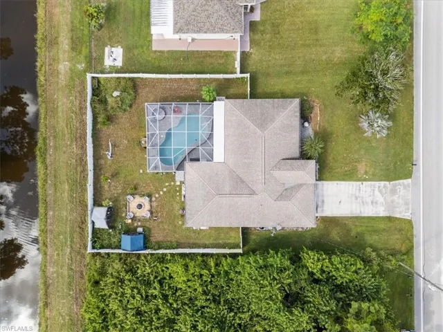 Aerial view showcasing a property with a distinct roofline, a screened-in swimming pool, a concrete driveway, and a fenced perimeter