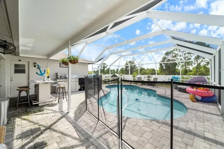 Screened lanai featuring a freeform swimming pool, paver deck, outdoor kitchen area, and privacy fencing