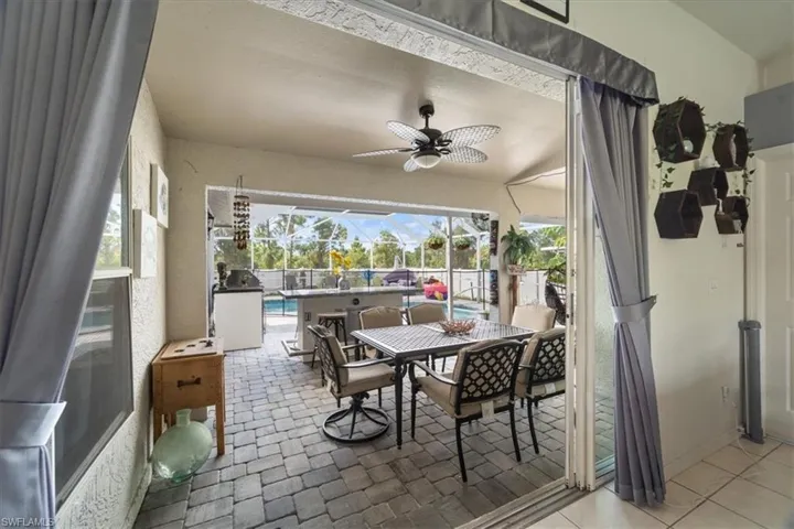 Screened patio featuring a paver floor, ceiling fan, built-in outdoor kitchen, and expansive pool deck with landscaping
