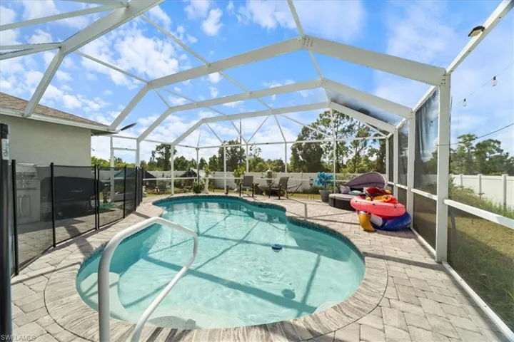Screened outdoor pool area featuring an in-ground swimming pool with handrails, surrounded by paver decking