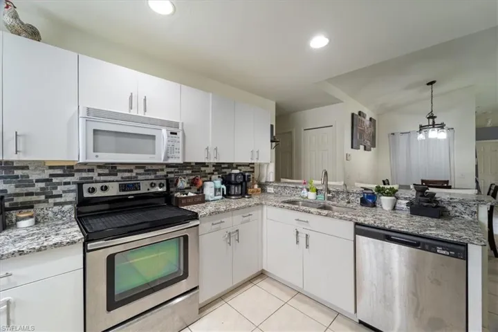 Modern kitchen featuring white cabinetry, stainless steel appliances, speckled stone countertops, a mosaic tile backsplash, and recessed lighting