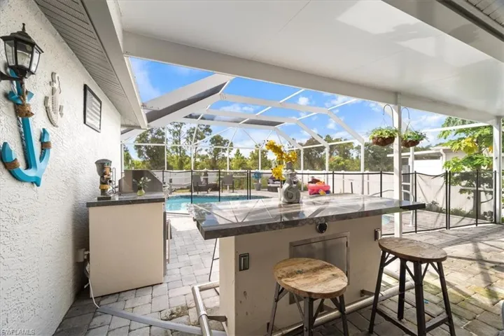 Screened-in outdoor living space featuring a built-in bar with stone countertop, paver flooring, and a fenced pool area