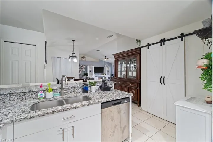 Kitchen featuring a double basin stainless steel sink, granite-style countertop, white cabinetry with brushed nickel hardware, and tile flooring