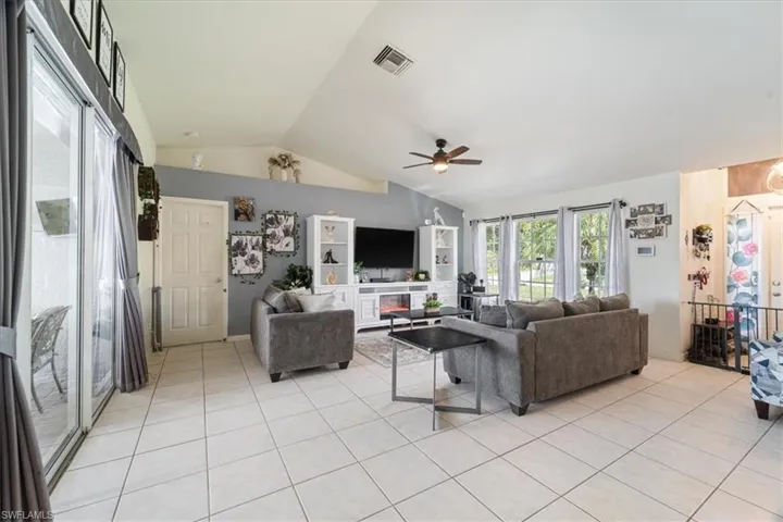 Spacious living area featuring light-toned tile flooring, vaulted ceilings, and a ceiling fan