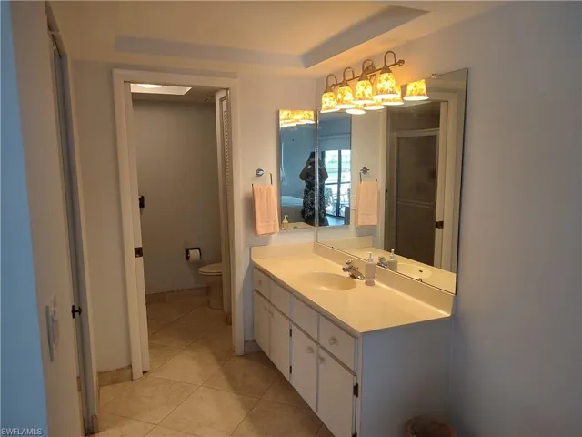 Bathroom with tile patterned flooring, toilet, vanity, and a tray ceiling