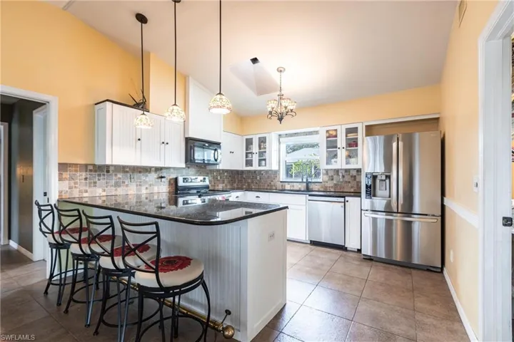 Kitchen featuring decorative backsplash, a peninsula, glass insert cabinets, white cabinets, and stainless steel appliances