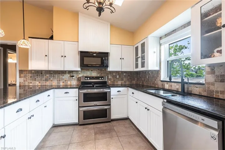Kitchen featuring stainless steel appliances, a chandelier, white cabinetry, and a sink