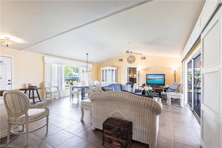 Living room featuring tile patterned flooring, visible vents, lofted ceiling, and ceiling fan with notable chandelier