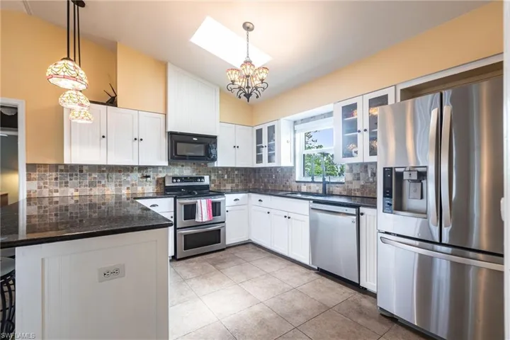 Kitchen featuring lofted ceiling, a peninsula, a chandelier, stainless steel appliances, and white cabinetry