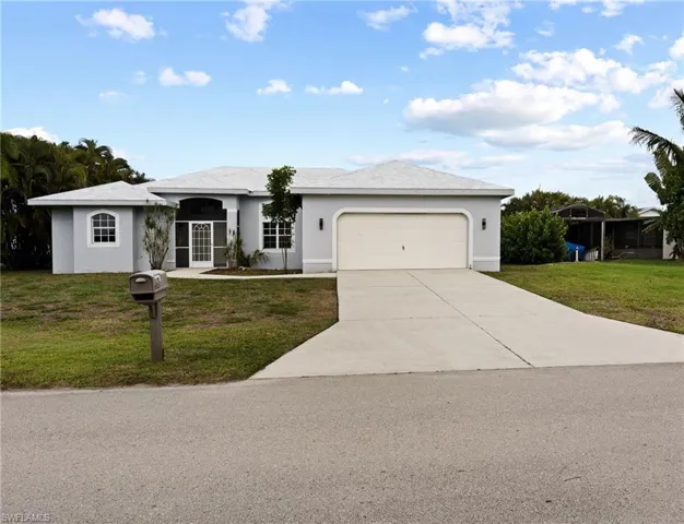 Single story home with a front yard, stucco siding, an attached garage, and concrete driveway