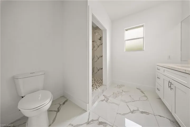 Bathroom featuring vanity, a marble finish shower, and light marble finish flooring