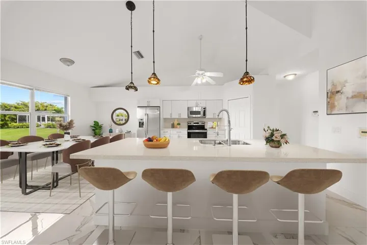 Kitchen with a kitchen bar, white cabinetry, stainless steel appliances, lofted ceiling, and decorative light fixtures