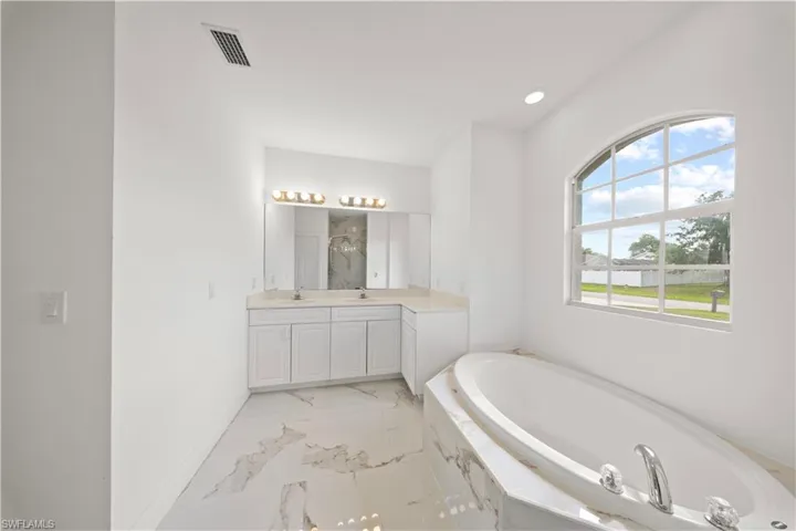 Bathroom with double vanity, a garden tub, light marble finish floors, and recessed lighting