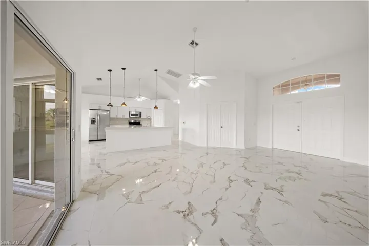 Unfurnished living room with a high ceiling, a ceiling fan, and light marble finish flooring