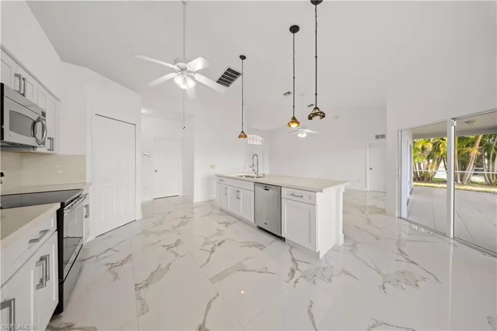 Kitchen featuring stainless steel appliances, white cabinetry, an island with sink, decorative light fixtures, and ceiling fan