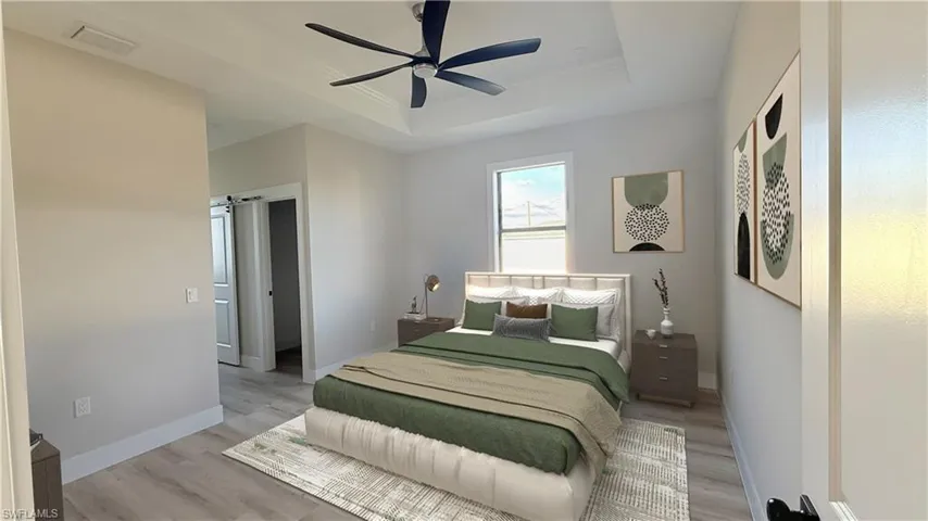 Master Bedroom featuring light wood finished floors, a ceiling fan, a barn door, and a raised ceiling. Staged picture