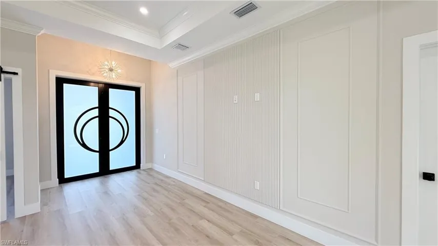 Foyer entrance with light wood finished floors, crown molding, a tray ceiling, recessed lighting, and a barn door