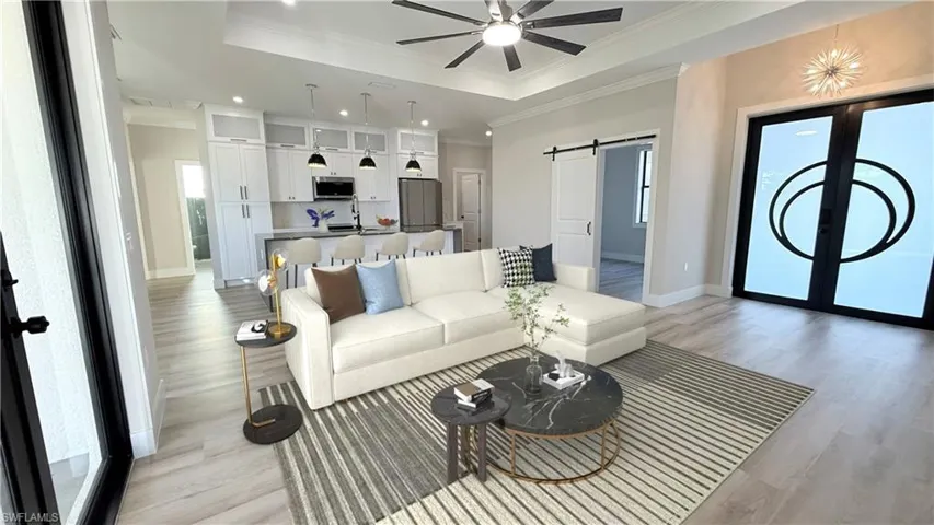 Living area with a barn door, a tray ceiling, recessed lighting, light wood-type flooring, and ceiling fan. Staged oicture