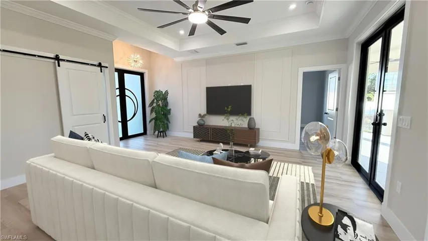 Living area with a barn door, french doors, light wood finished floors, crown molding, and recessed lighting. Staged picture