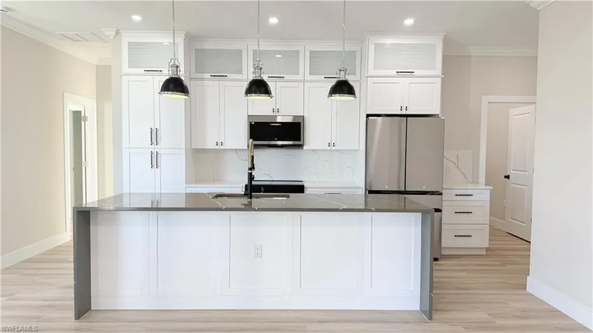 Kitchen with ornamental molding, dark stone counters, white cabinetry, an island with sink, and stainless steel appliances