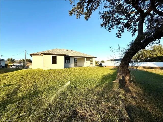 Back of property featuring stucco siding, a lawn, and a shingled roof