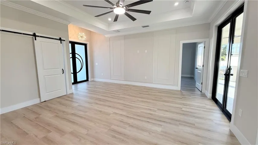 Unfurnished bedroom featuring a barn door, access to outside, french doors, light wood-type flooring, and ceiling fan