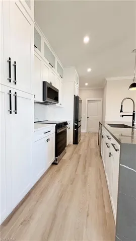 Kitchen with glass insert cabinets, ornamental molding, pendant lighting, light wood-style floors, and white cabinetry