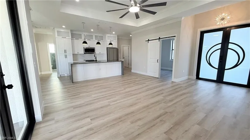 Kitchen featuring open floor plan, white cabinets, glass insert cabinets, a barn door, and an island with sink