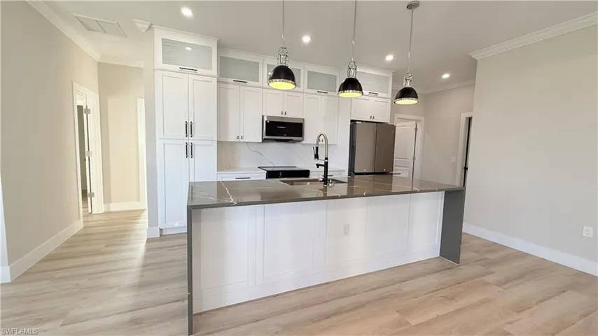 Kitchen featuring white cabinets, stainless steel appliances, pendant lighting, light wood-type flooring, and crown molding