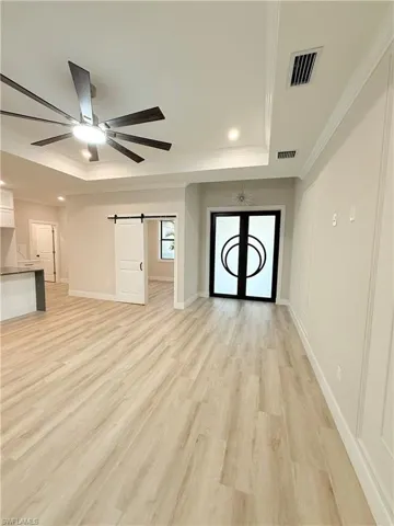Unfurnished living room featuring a barn door, light wood-style flooring, a raised ceiling, ornamental molding, and ceiling fan