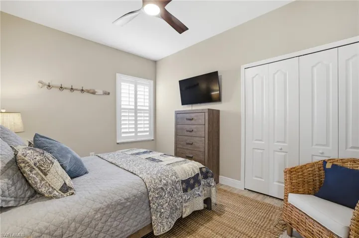 Bedroom featuring plantation shutters, wood-finish flooring, a ceiling fan with integrated lighting, and bi-fold closet doors