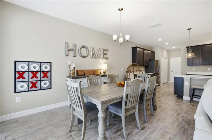 Open-concept living space featuring wood-finish tile flooring throughout, a dining area with a chandelier, and a kitchen with dark cabinetry and light countertops