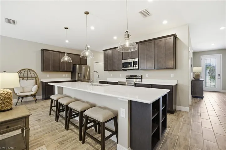 Kitchen featuring a large central island with seating, dark wood cabinetry, stainless steel appliances, and white countertops